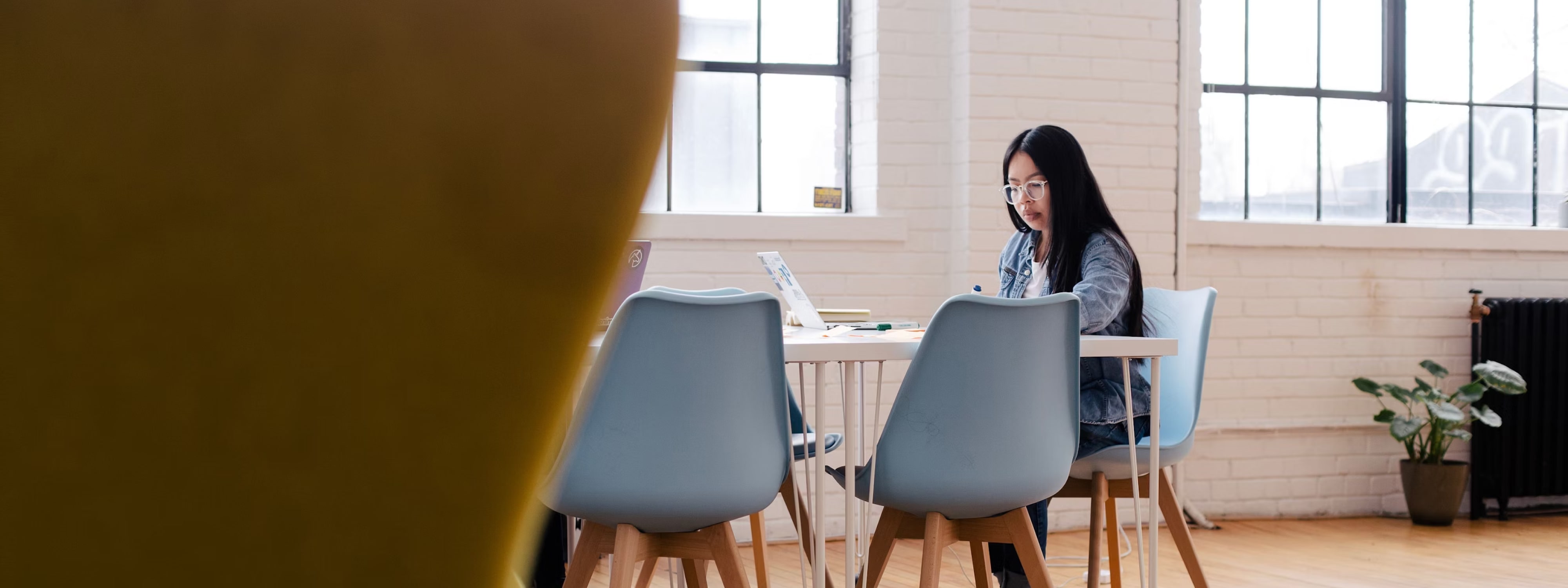 Woman working on laptop at minimalist wooden table with blue chairs