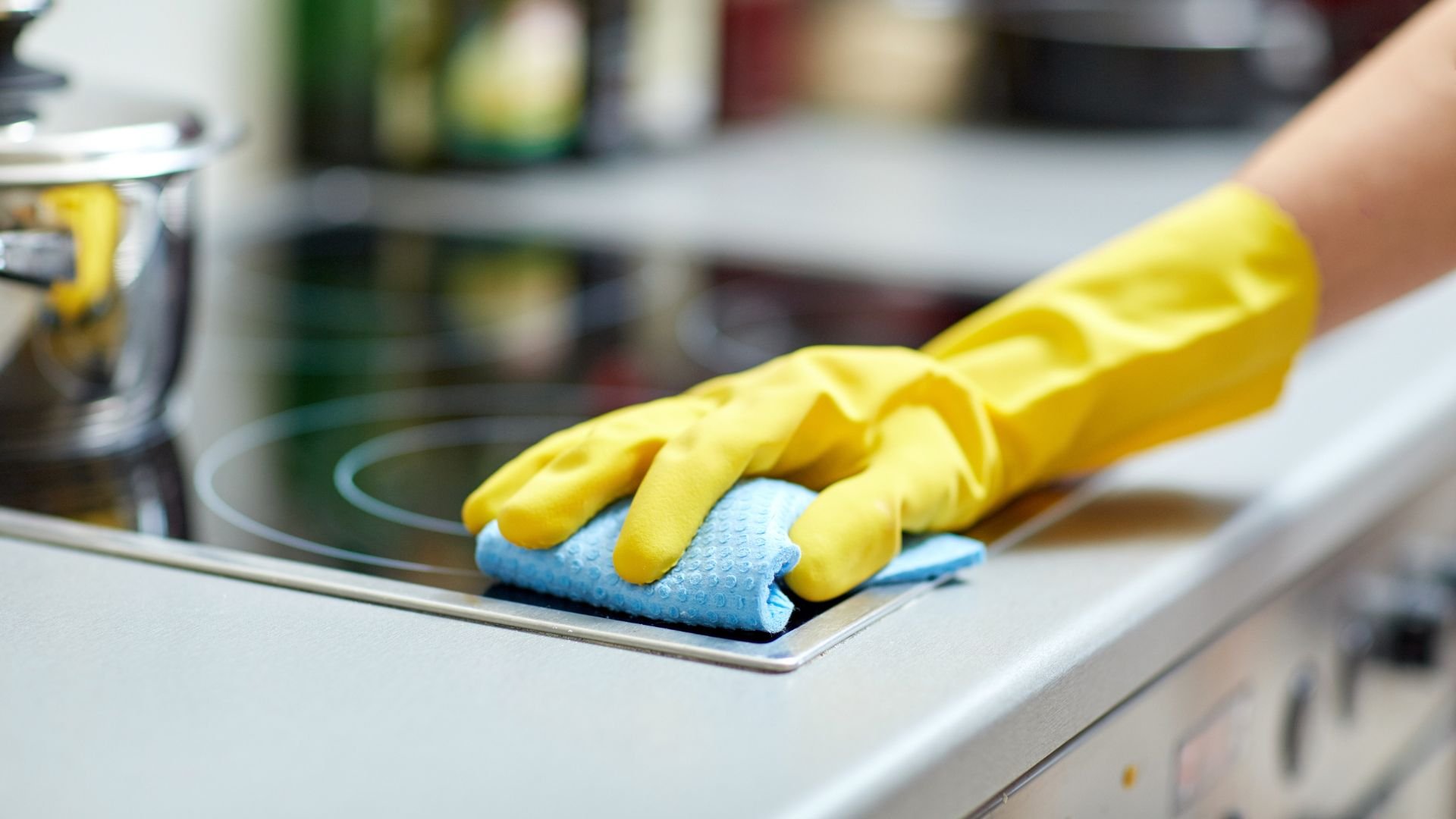 Yellow gloved hand cleaning kitchen surface with blue microfiber cloth