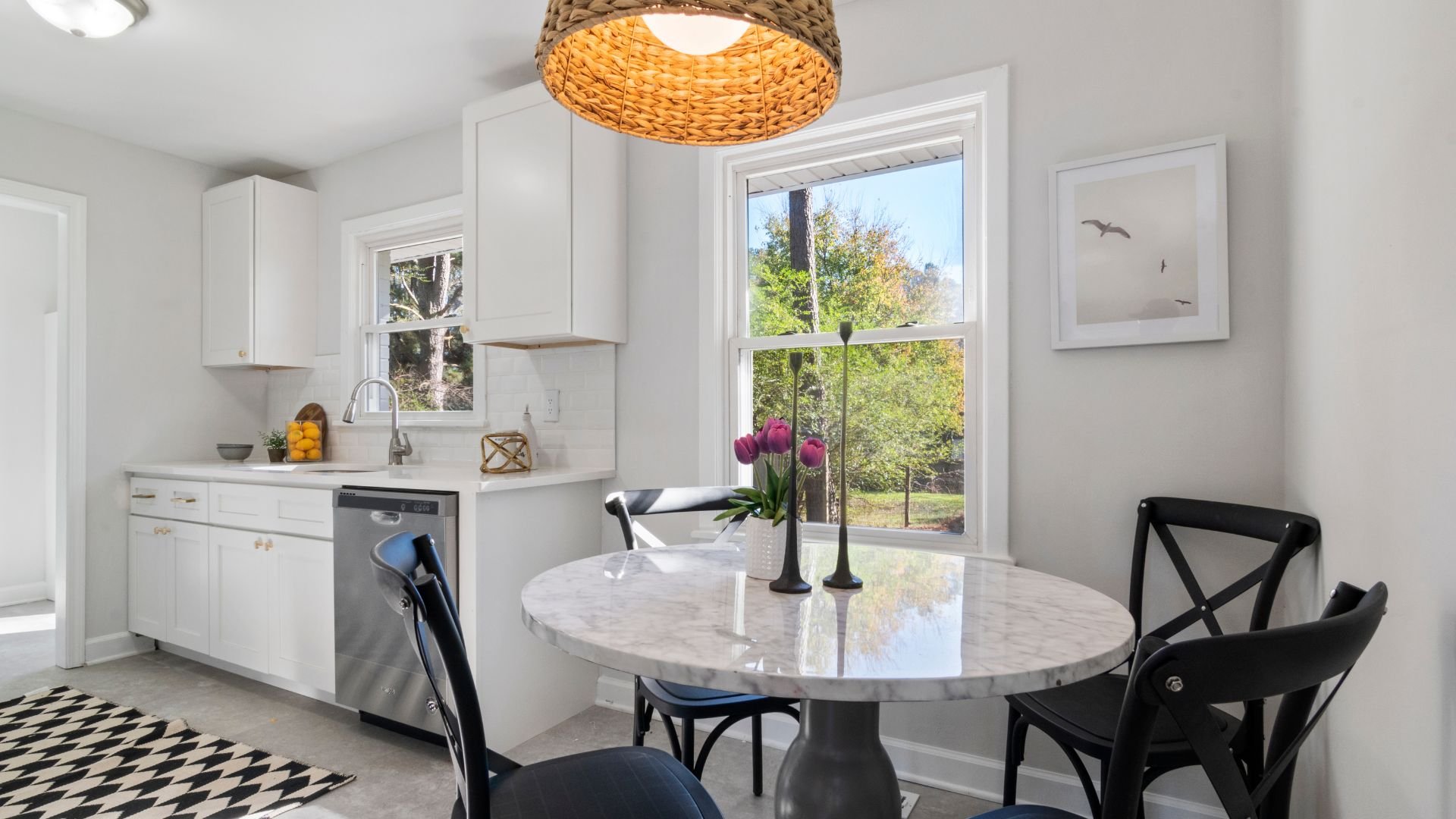 Bright white kitchen with marble table, black chairs, and woven lamp shade