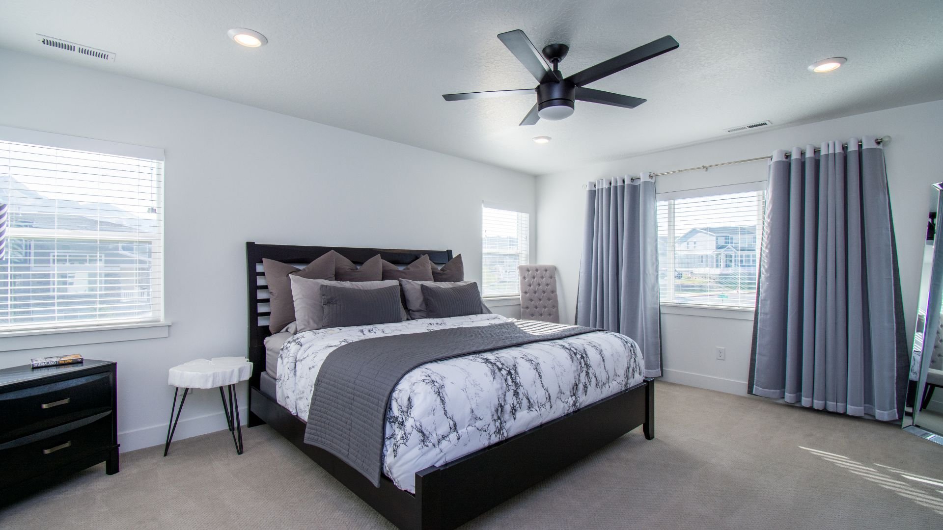 Modern bedroom with marble bedding, gray curtains, and ceiling fan
