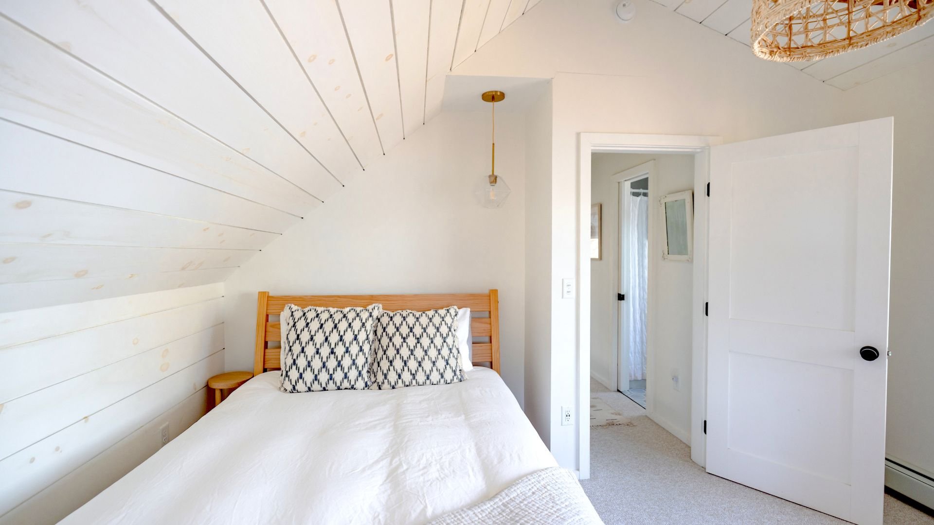 Bright, minimalist bedroom with white walls, wooden bed, and geometric pillows